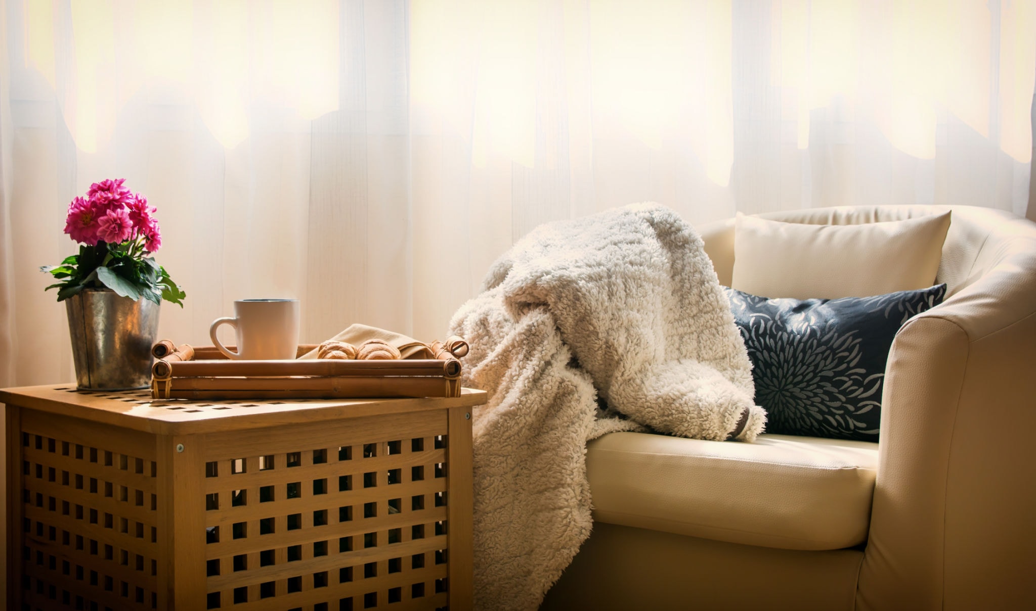 Cosy armchair with a soft blanket, a mug, and fresh flowers by a sunlit window