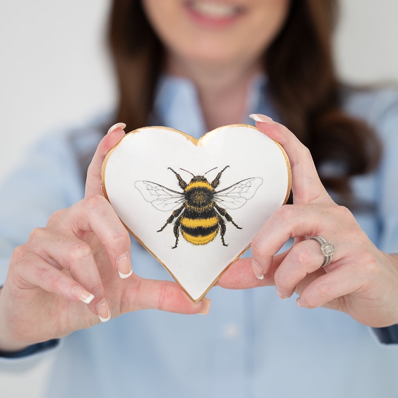 Andrea O'Reilly holding a heart-shaped ceramic with a bee illustration